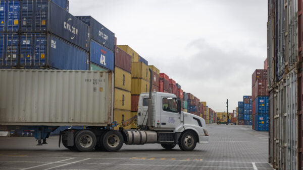 A sixteen-wheel truck driving in front of containers at a port