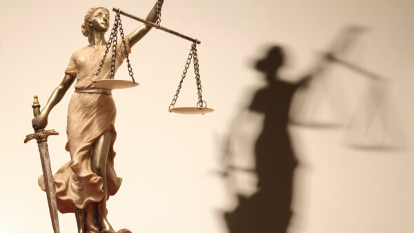 Small gold statue of Lady Justice against a tan background with Lady Justice's shadow