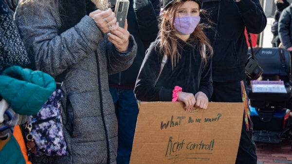 Rent-control advocates stand behind cardboard rally sign