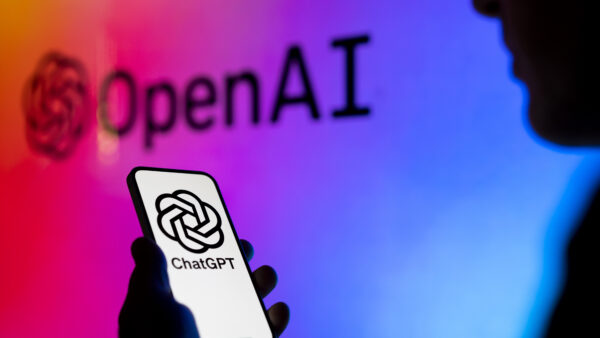 A phone with a floral black and white ChatGPT graphic on it held by a shadowy figure against a rainbow OpenAI background