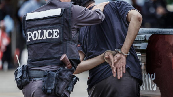 A police officer guides a suspect who is handcuffed behind his back.