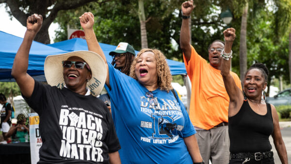 Black voters cheer at an NAACP voting rights rally. One woman is wearing a shirt that says "BLACK VOTERS MATTER"