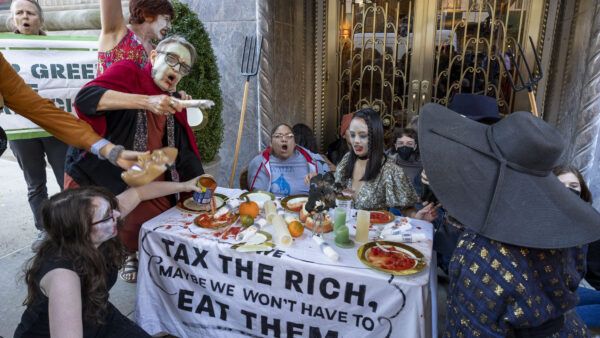 A group of protestors standing around a table that has a tablecloth reading "Tax the Rich"