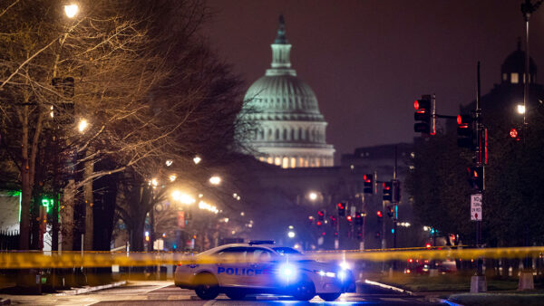 A photo of the U.S. Capitol at night with a police car blocking the street in the foreground