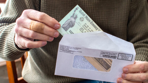 A man in a ribbed green sweater opens an envelope and takes out a Treasury check for COVID-19 pandemic stimulus.