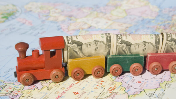 A toy train moves across a map of Asia, loaded with rolled-up U.S. $10 bills as its cargo.