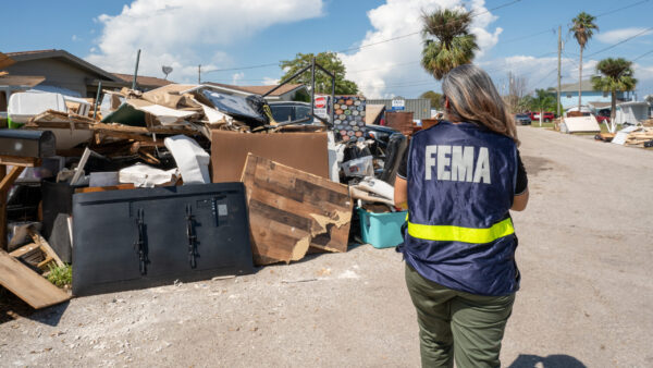 A person in a FEMA vest walking through a recent disaster zone.