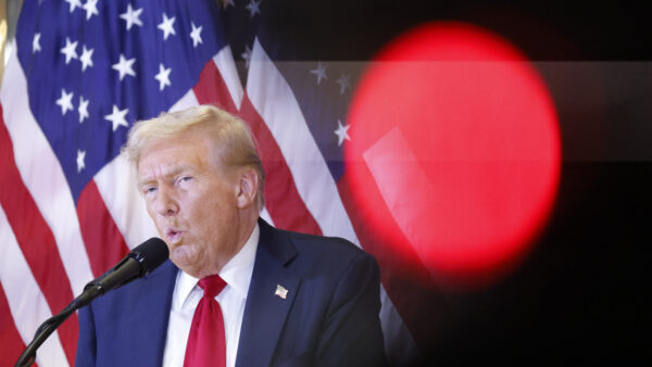 Former President Donald Trump in front of an American flag, speaking at a press conference.