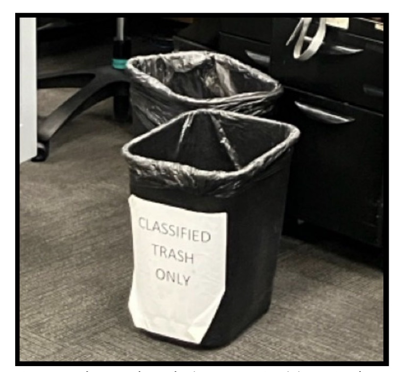 A blurry photo from the TIGTA report of an open trash can with a sign on the side reading "CLASSIFIED TRASH ONLY." | U.S. Treasury Department Inspector General for Tax Administration